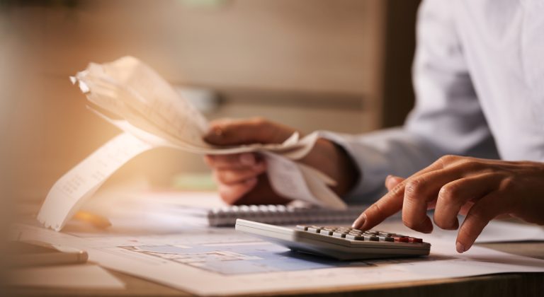 Close-up of economist using calculator while going through bills and taxes in the office.